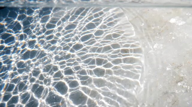 Water caustics project bright web patterns over a light sandy floor in clear shallow pool water.