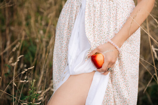 Woman holding a red apple in her hand while standing in a field during a sunny day