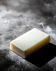 Fototapeta premium Elegant natural soap bar, dramatically lit to emphasize its smooth texture and pristine form, casting a profound shadow on a dark, industrial concrete surface