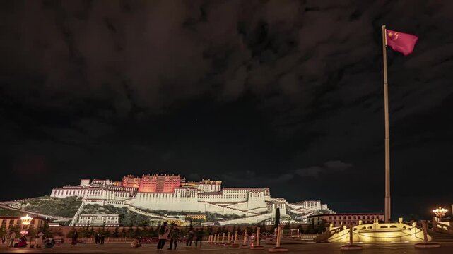 Potala Palace illuminated at night in Lhasa with Chinese national flag waving in foreground