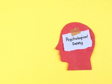 Psychological safety phrase on paper taped to red head silhouette on yellow background. Concept for mental health, workplace culture, brain wellness, psychology, trust, and employee support