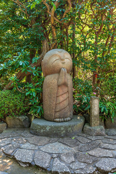 Smiling stone Jizo statue in green garden at Hase-dera temple in Kamakura Japan