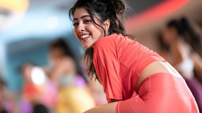Happy young woman smiling warmly while wearing comfortable coral sportswear during an intense fitness group exercise class inside modern gym