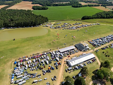 Aerial view of the Bad Apples PPG Fly-in at Hodges Field with paragliders in the sky and numerous RVs and vehicles parked in the grassy field in Andersonville, Georgia, United States.