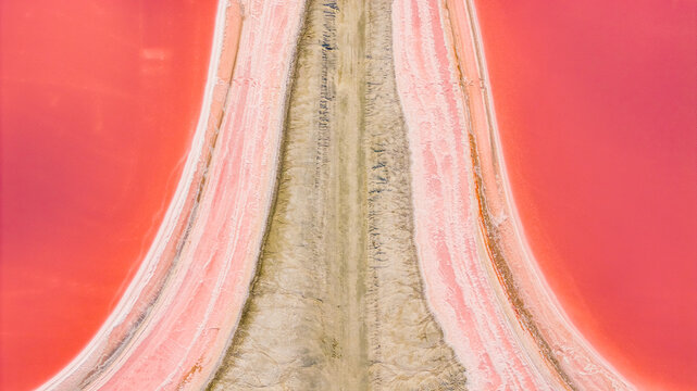 Aerial view of vivid pink salt evaporation ponds and crystallized salt banks forming a geometric landscape at the industrial saltworks in Aigues-Mortes, Occitanie, France.