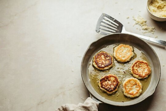 Potato latkes frying in shallow oil in a stoneware pan beside a slotted turner