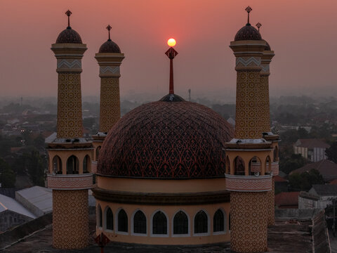 Aerial view of a mosque dome and minarets at sunset featuring intricate patterns and warm light over the urban landscape of Klaten, Central Java, Indonesia.