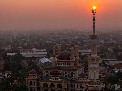 Aerial view of the Grand Mosque of Klaten with its prominent minaret and domes illuminated by the warm glow of the setting sun over the urban landscape in Klaten, Central Java, Indonesia.