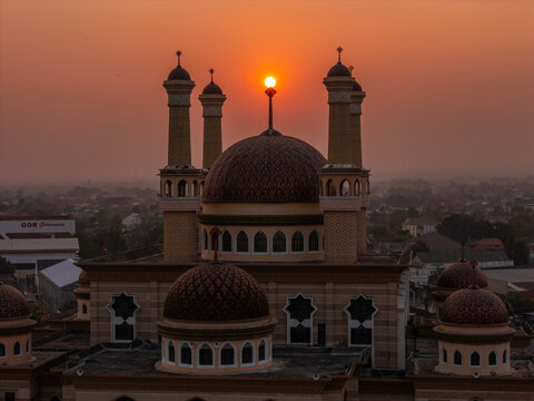 Aerial view of the Grand Mosque of Klaten with its ornate domes and minarets silhouetted against a vibrant sunset sky, Klaten, Central Java, Indonesia.