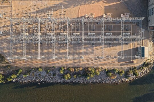 Aerial view of an electrical power substation with metal structures, transformers, and power lines located near a rocky shoreline and water in Estes Park, Colorado, United States.