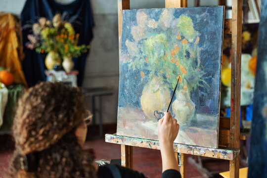 Learning painting. Teenage girl paints still life on canvas with oil paints, holds brush, palette.