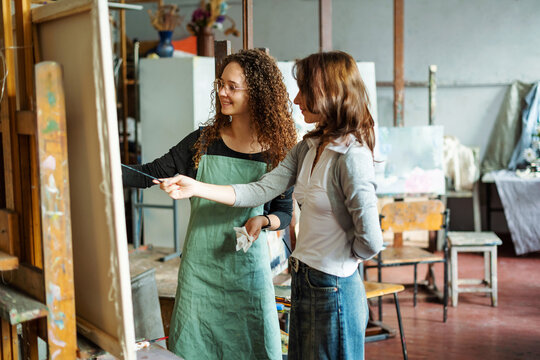 Two teenage girls in college painting class, painting still life on canvas with oil paints, holding brush, palette. Art studio, art workshop.