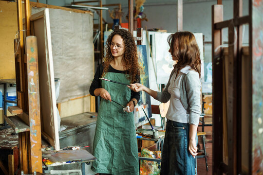 Two teenage girls in college painting class, painting still life on canvas with oil paints, holding brush, palette. Art studio, art workshop.