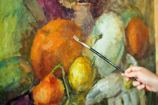 Close-up of hand holding brush and painting with paints on canvas. Art studio, art workshop. Painting class, painting still life on canvas with oil paints