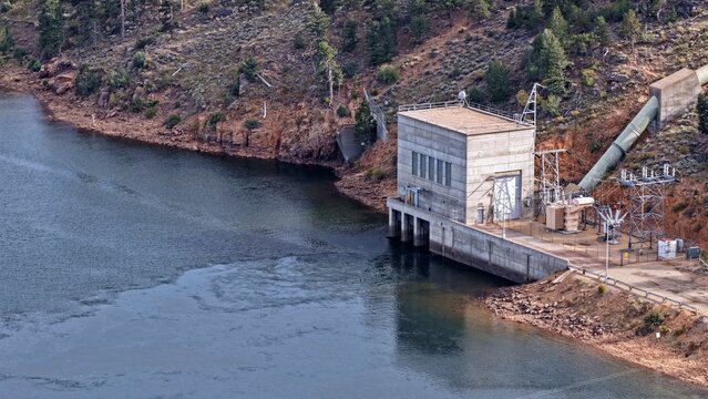 Aerial view of the hydroelectric power plant facility situated on the edge of a reservoir with a large water pipe and concrete structure in Estes Park, Colorado, United States.