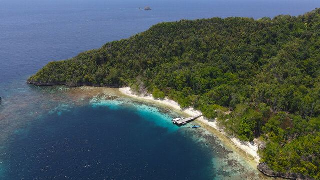 Aerial view of Piaynemo with a wooden jetty in turquoise waters, surrounded by dense tropical rainforest and rugged coastline in Raja Ampat, Southwest Papua, Indonesia.
