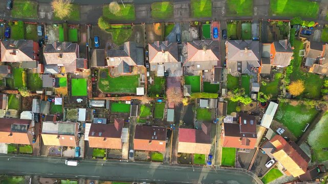 Vertical drone view above rows of English homes with green gardens, backyards, rooftops and residential streets forming a geometric suburban pattern, 4K.