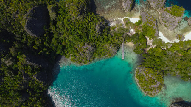 Aerial view of the karst islands and turquoise lagoon at Piaynemo with a wooden jetty surrounded by dense tropical vegetation in Raja Ampat, Southwest Papua, Indonesia.
