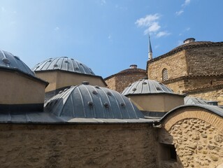 A low-angle professional travel photograph of traditional Turkish bath (hammam) domes against a beautiful blue sky with soft white clouds. The ancient stone and brick textures of the domes are highly  © kamchoo