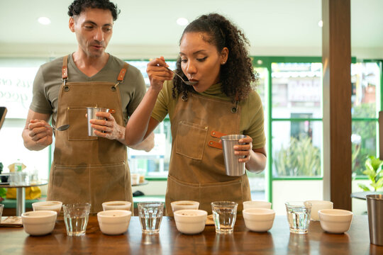 Two coffee professionals tasting multiple coffee samples with spoons during a sensory evaluation session in a specialty coffee shop