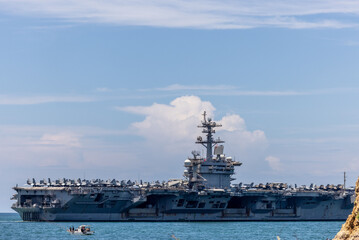 US Navy aircraft carrier USS Abraham Lincoln CVN 72 is anchored at sea. Military jets are parked on USS Abraham Lincoln. Small boat passes near USS Abraham Lincoln. © Nutchanart