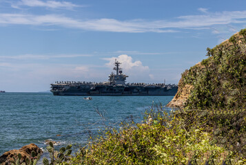 US Navy aircraft carrier USS Abraham Lincoln CVN 72 is anchored at sea. Military jets are parked on USS Abraham Lincoln. Small boat passes near USS Abraham Lincoln. © Nutchanart