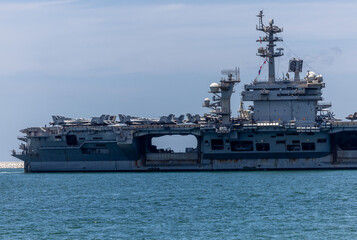 US Navy aircraft carrier USS Abraham Lincoln CVN 72 is anchored at sea. Military jets are parked on USS Abraham Lincoln. Small boat passes near USS Abraham Lincoln. © Nutchanart