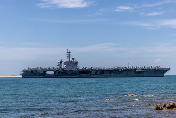 US Navy aircraft carrier USS Abraham Lincoln CVN 72 is anchored at sea. Military jets are parked on USS Abraham Lincoln. Small boat passes near USS Abraham Lincoln. © Nutchanart