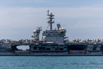 US Navy aircraft carrier USS Abraham Lincoln CVN 72 is anchored at sea. Military jets are parked on USS Abraham Lincoln. Small boat passes near USS Abraham Lincoln. © Nutchanart