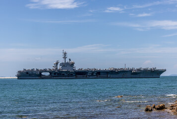 US Navy aircraft carrier USS Abraham Lincoln CVN 72 is anchored at sea. Military jets are parked on USS Abraham Lincoln. Small boat passes near USS Abraham Lincoln. © Nutchanart