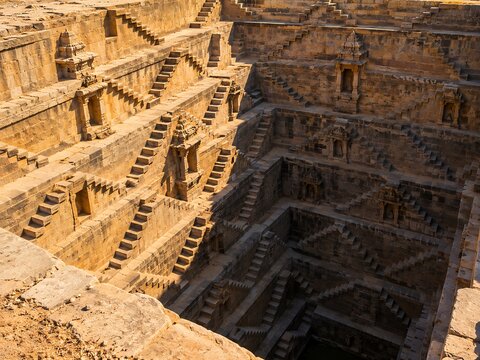 An ancient stone stepwell with intricate geometric stairs leading down to the bottom in a historic architectural site under bright sunlight