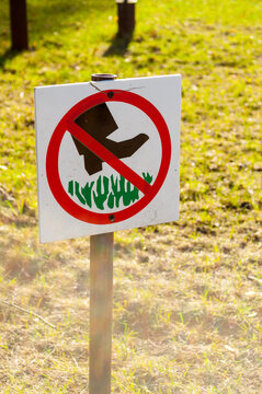 Sign Do not walk the lawn. A square prohibition sign on a metal pole - a red circle with a black boot symbol and green grass icons on a blurred park background