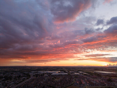 Aerial view of the town of Stafford at sunset, with vibrant pink and orange clouds filling the sky above residential areas and industrial buildings in Stafford, England, United Kingdom.