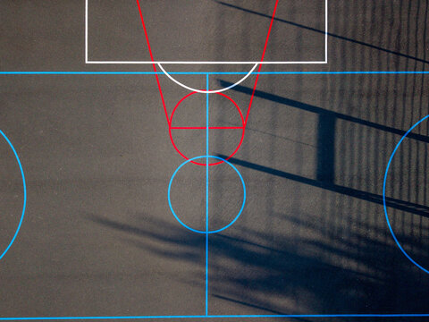 Aerial view of the basketball court at Wildwood Park with colorful court markings on a dark surface and long shadows cast across the ground in Stafford, England, United Kingdom.