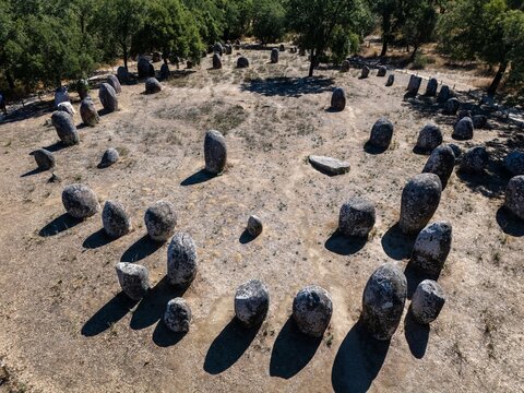 Aerial view of Almendres Cromlech, a prehistoric megalithic site with ancient stone monoliths in a circle, surrounded by trees in Nossa Senhora de Guadalupe, Distrito de Evora, Portugal.