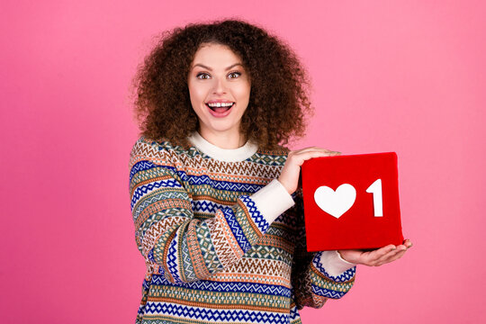 Happy young woman holding a red heart like notification cube, smiling portrait for social media, influencer concept, engagement and positive digital communication in studio on pink background