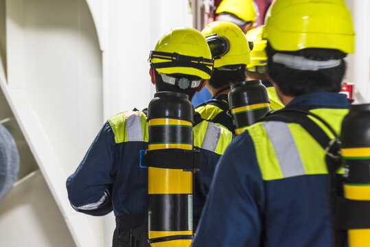Commercial vessel crew preparing for an emergency response exercise, with several seafarers equipped with SCBA sets and compressed-air bottles.