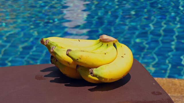 Ripe Yellow Bananas Rest on a Pool Surface Beside Rippling Blue Water, Evoking Freshness and Healthy Eating