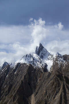 Aerial view of Uli Biaho Tower, a dramatic granite monolith mountain with snow-capped peaks and rocky slopes under a blue sky in Skardu, Pakistan.