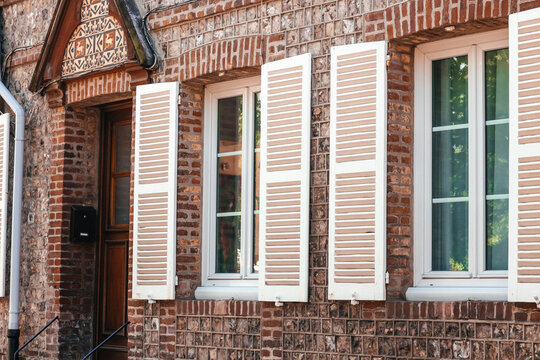 Brick building exterior featuring white wooden shutters and large windows, showcasing detailed architectural elements and a warm, inviting facade in a residential area