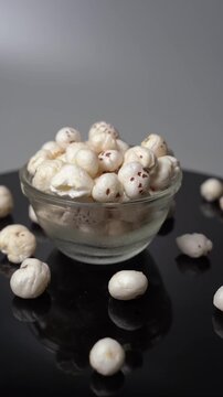 Fox nut, Euryale ferox, lotus seed snack in glass bowl on dark reflective surface, healthy plant based dry fruit food product video