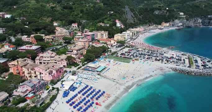 Beachfront Monterroso al Mare town in Cinque Terre, Italy, captures a vibrant summer scene with tourists relaxing on the sandy shores under umbrellas