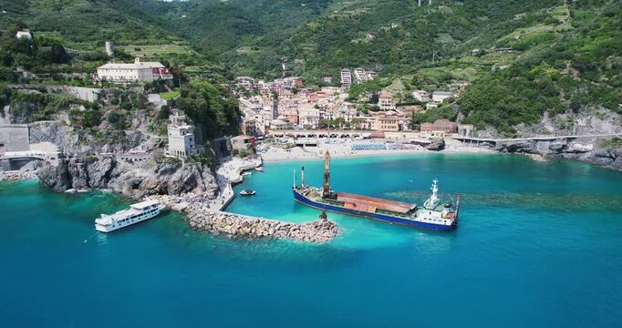 Industrial vessel equipped with a digger operates near the beach coastline of Monterosso al Mare in Cinqu Terre, Italy