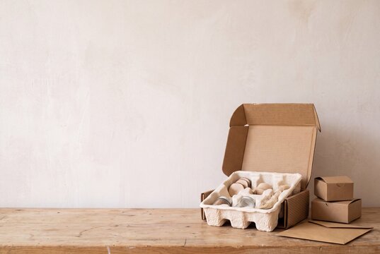 Open eco friendly cardboard packaging box with molded pulp insert and sustainable materials on wooden table against neutral wall