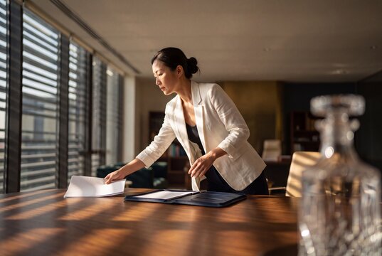 Asian businesswoman preparing documents and folder on a wooden conference table in a modern corporate office