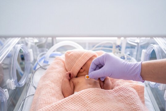 Doctor or nurse placing a medical sensor on a premature newborn baby inside an incubator in the neonatal intensive care unit