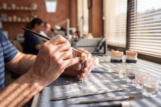 Dental technician applying ceramic porcelain layer to a tooth crown prosthesis using a fine brush in a laboratory