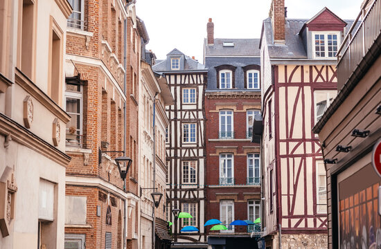 Historic European street view featuring half-timbered buildings and colorful umbrellas in a charming alleyway of a French city during daytime