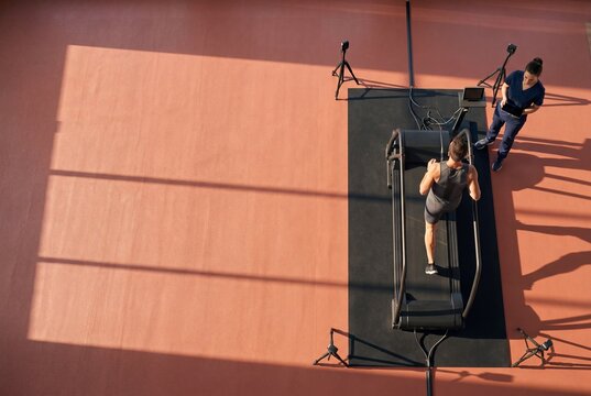 Top view of a male athlete running on a treadmill during a sports science biomechanics test monitored by a female trainer