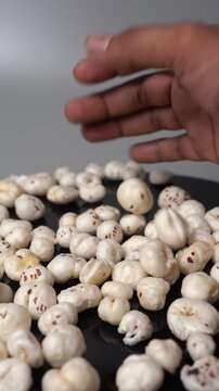 Close-up of human hand pick and drop puffed fox nut, Euryale ferox, or makhana on black table in studio background video clip